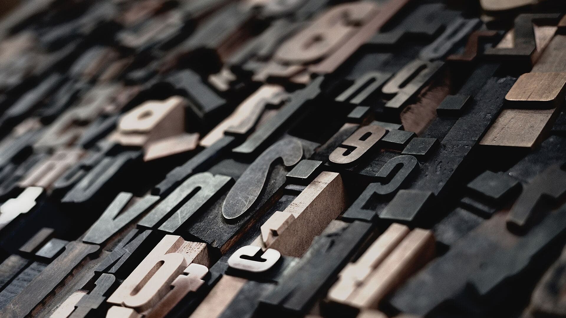 A type case filled with wooden letterpress type, seen from a low angle: rows of raised wooden letters and numerals, most of them inked dark grey, a few still bare wood.