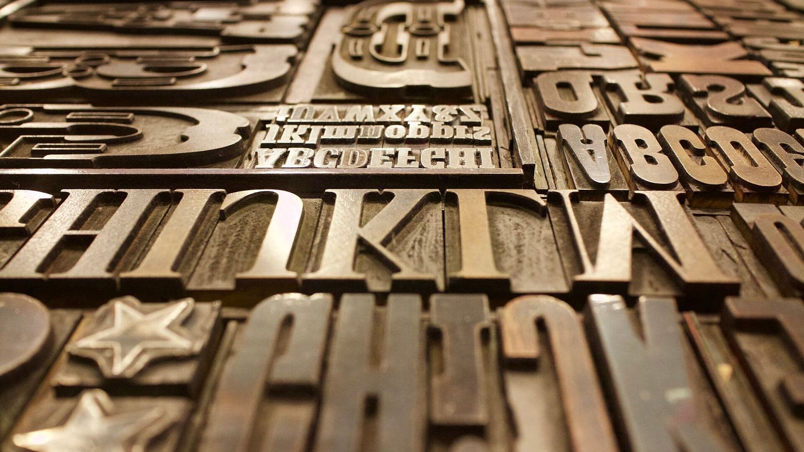 Large wooden display letters, including the word THINK and two star shapes, packed into a letterpress type case shown close up.