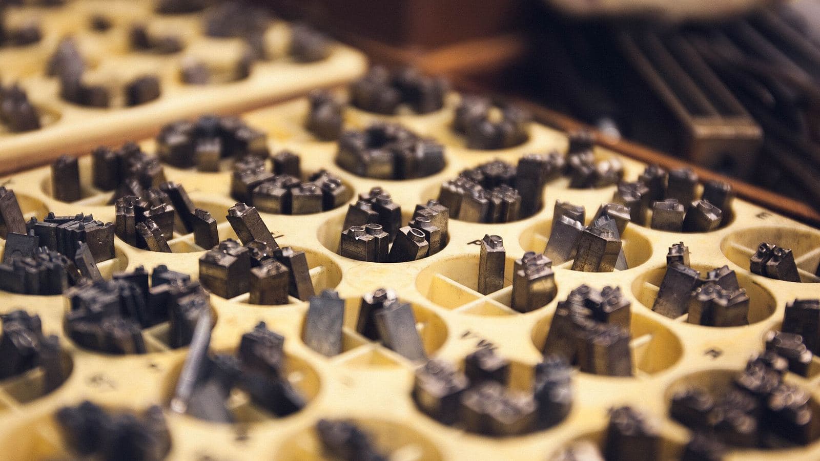 Individual metal type sorts standing upright in the compartments of a cream-coloured tray, photographed from above.